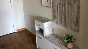 Un pasillo con pared de madera rústica, una puerta blanca, un mueble blanco con cajones y un estante con plantas en macetas.