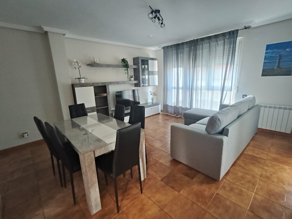 A modern living room with a dining area, grey sofa, and a TV.