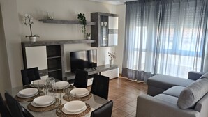 Una sala moderna con comedor, sofá gris, televisor y plantas decorativas.