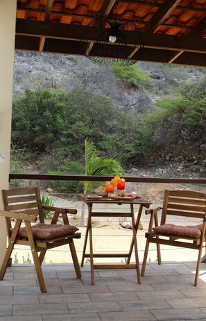 Un patio con dos sillas de madera y una mesa con una bebida y fruta.