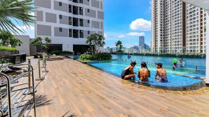 A swimming pool area with a wooden deck, metal railings, and a view of high-rise buildings in the background. - Apartment Pool Infinity View HCM (Ho Chi Minh City)