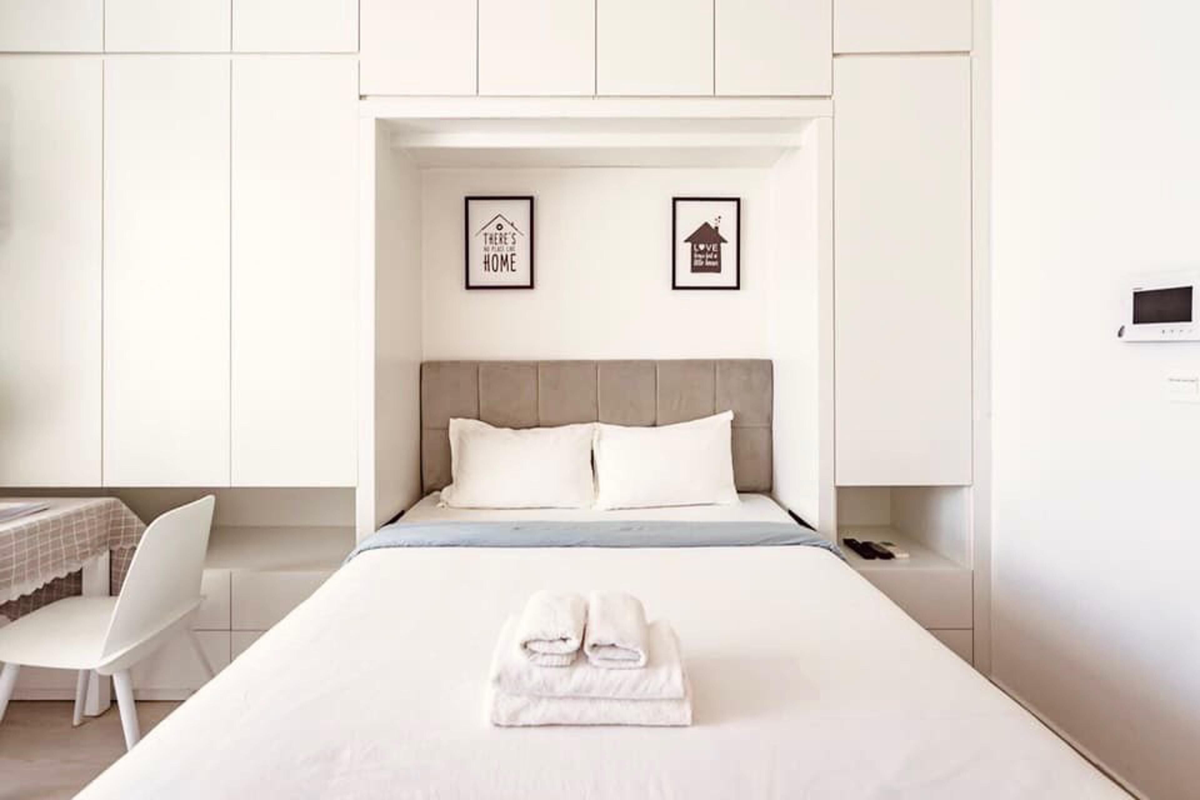 Ein ordentlich eingerichtetes Schlafzimmer mit einem Bett, Kissen, einem Nachttisch, einem Sessel und zwei gerahmten Bildern an der Wand.