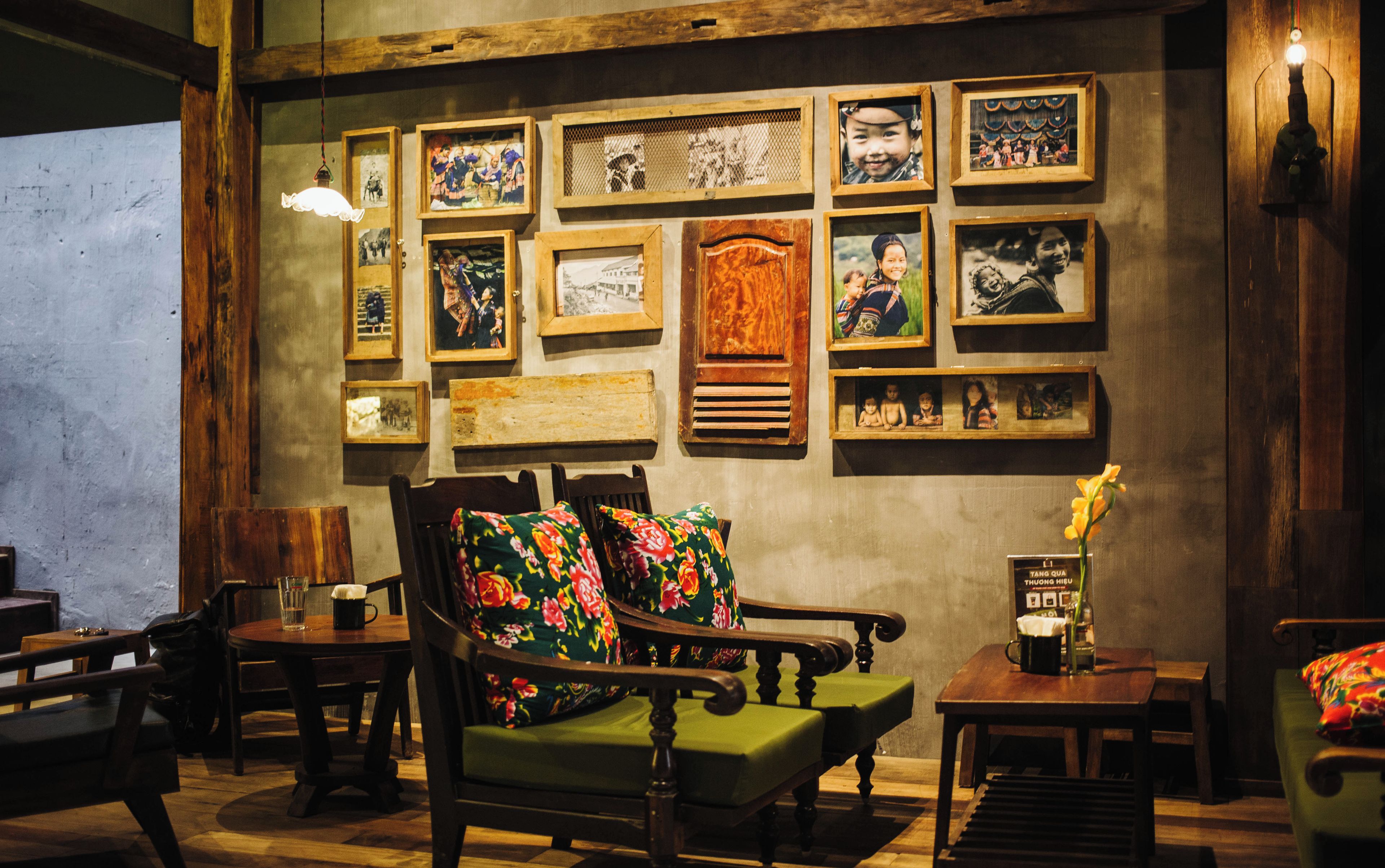 A cozy room with a wooden sofa, a small table with a vase of flowers, and a wall adorned with framed pictures.