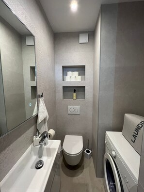 A compact bathroom with a sink, toilet, and washing machine.