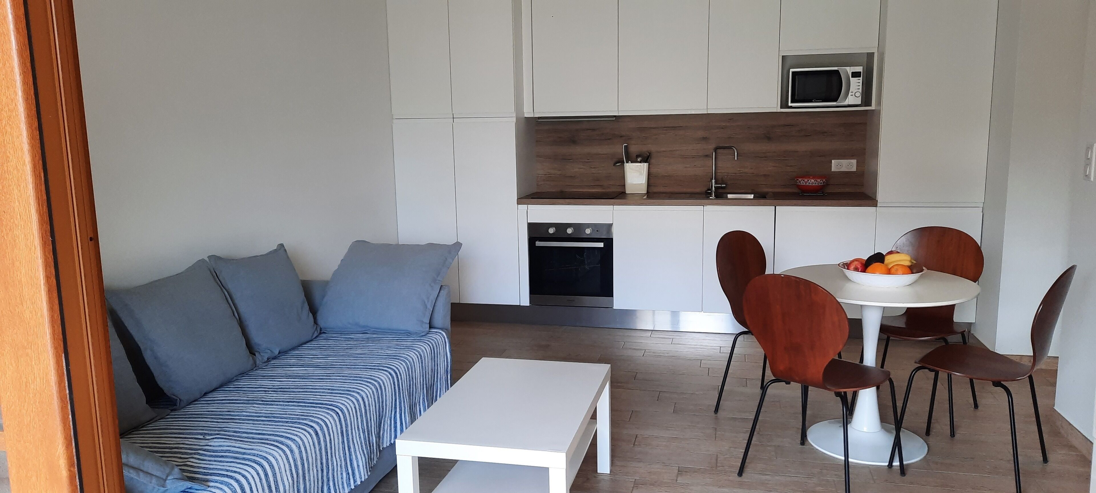 Um espaço de estar compacto com sofá, mesa de jantar e área de cozinha, incluindo micro-ondas e pia.