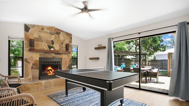 A room with a ping pong table, stone fireplace, wicker chairs, and a view of the backyard.