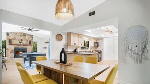 A modern kitchen with a stone fireplace, yellow chairs, and a dining area with a wooden table.