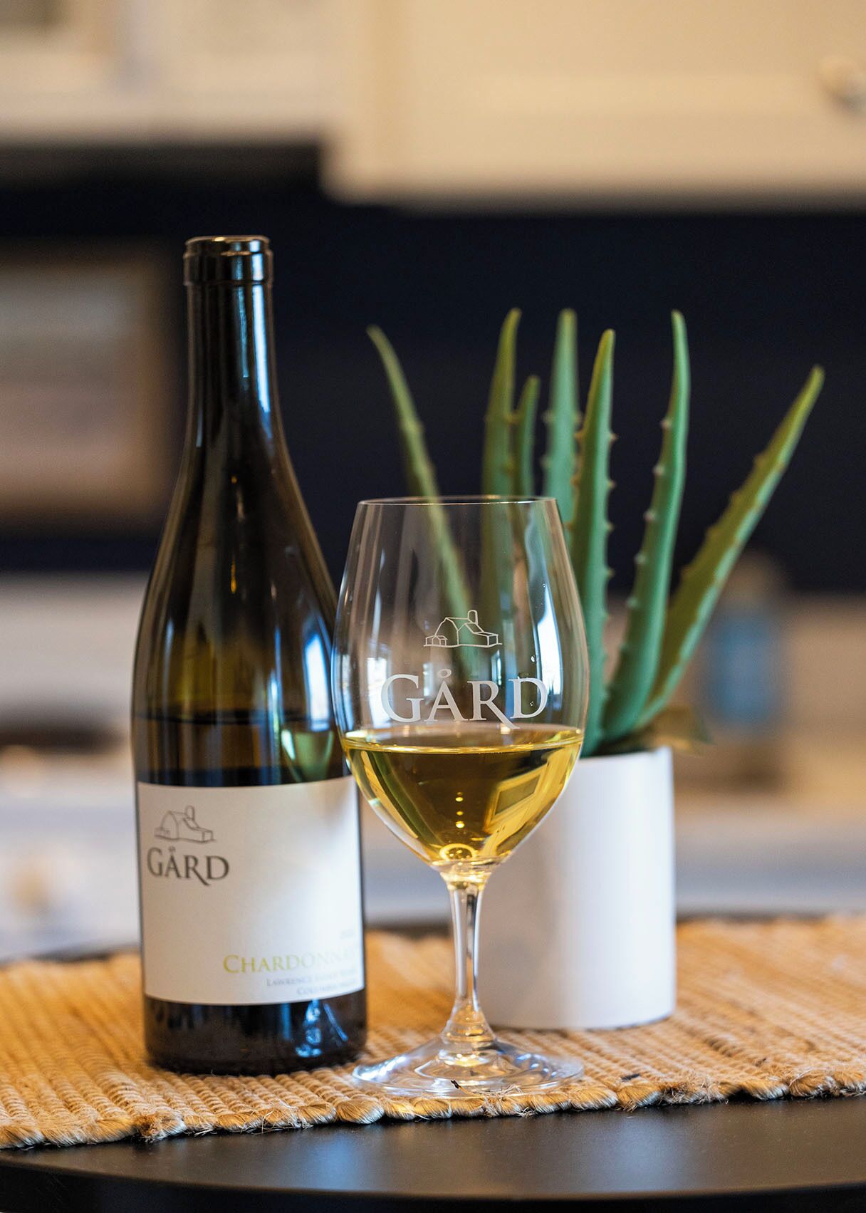 A bottle of Charles Garnier wine and a glass of white wine on a table with a woven placemat.