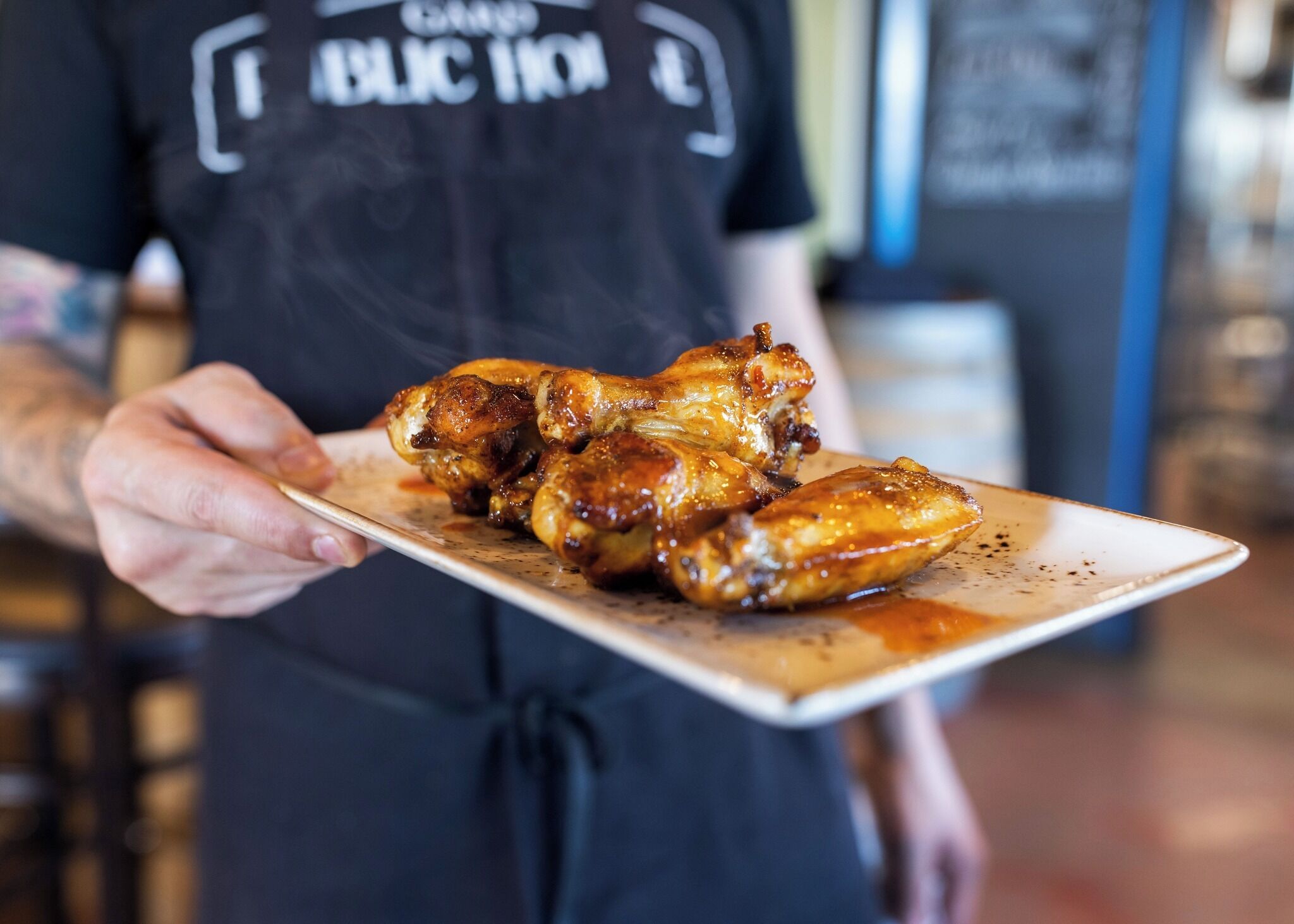A person holding a plate of glazed chicken wings.