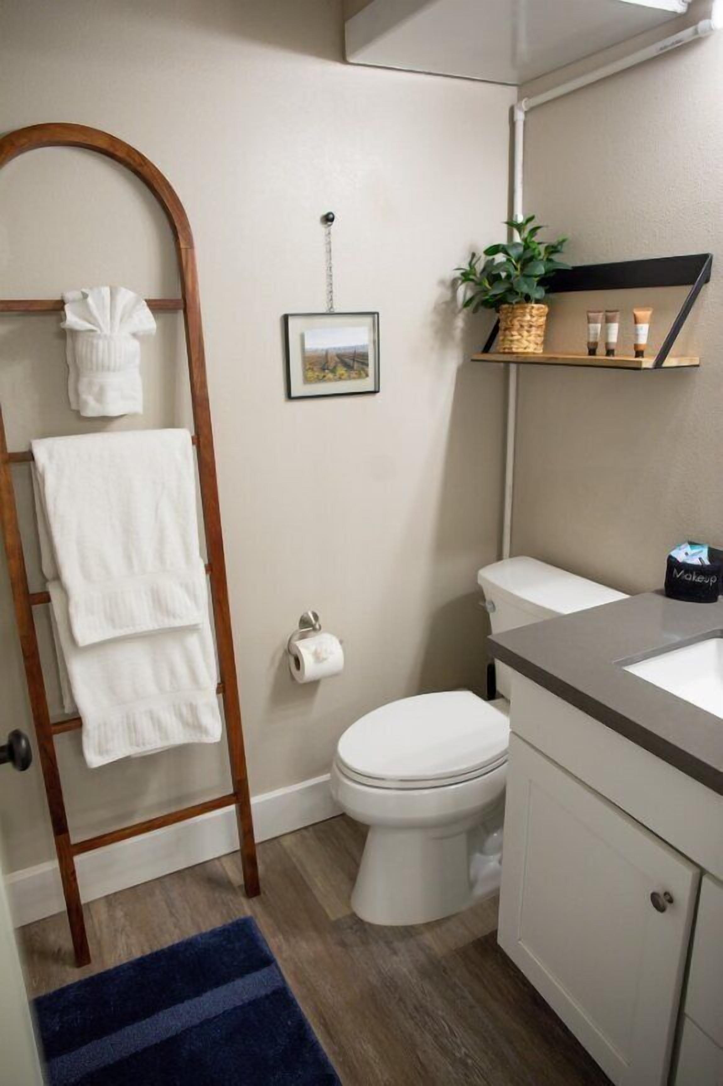 A bathroom with a wooden towel rack, a toilet, a sink, and a small shelf with toiletries.