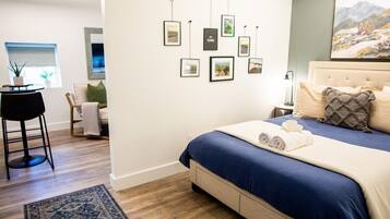 A modern bedroom with a bed, a wall-mounted picture gallery, a small side table with a plant, and a view of a room with a window.