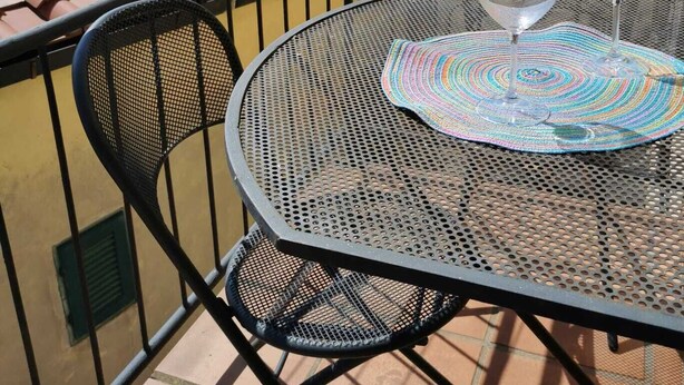 A balcony with a round metal table and two wine glasses, overlooking a cityscape with terracotta roofs and a clock tower. - 1 Bedroom Apartment in Capoliveri (Capoliveri)