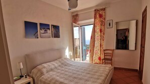 A bedroom with a bed, a nightstand, a chair, a ceiling fan, and a balcony with a view. - 1 Bedroom Apartment in Capoliveri (Capoliveri)