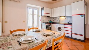 A compact kitchen with white cabinets, a washing machine, and a dining area with a table set for four. - 1 Bedroom Apartment in Capoliveri (Capoliveri)
