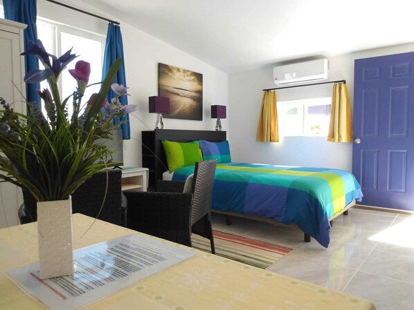 Habitación de hotel con cama, escritorio, silla, ventana con cortinas y puerta.