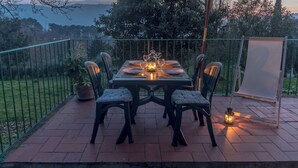 Een terras buiten met een eettafel, omringd door stoelen en een lantaarn voor licht.
