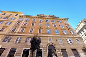 Un immeuble à plusieurs étages, de style architectural classique, avec une entrée centrale surmontée d’une grande porte en arc de cercle et d’une enseigne.