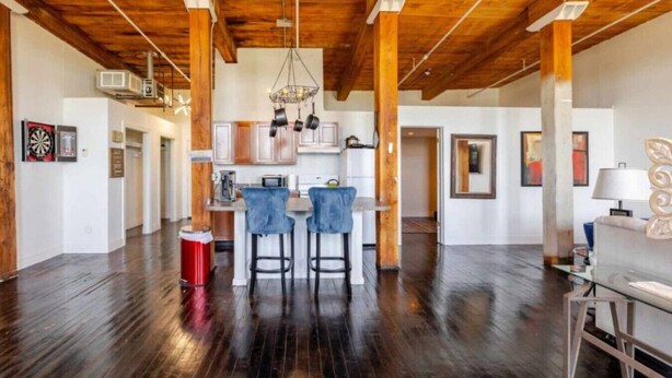 A spacious kitchen with wooden beams, a central island with bar stools, and a red cooler. - Fun Loft with Arcade Games and River Views (Detroit)