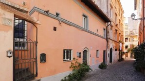 A narrow cobblestone street flanked by buildings with arched windows and a small garden area. - Delightful apartment in Trastevere on two levels MauveSweetRhome 3 (Roma)
