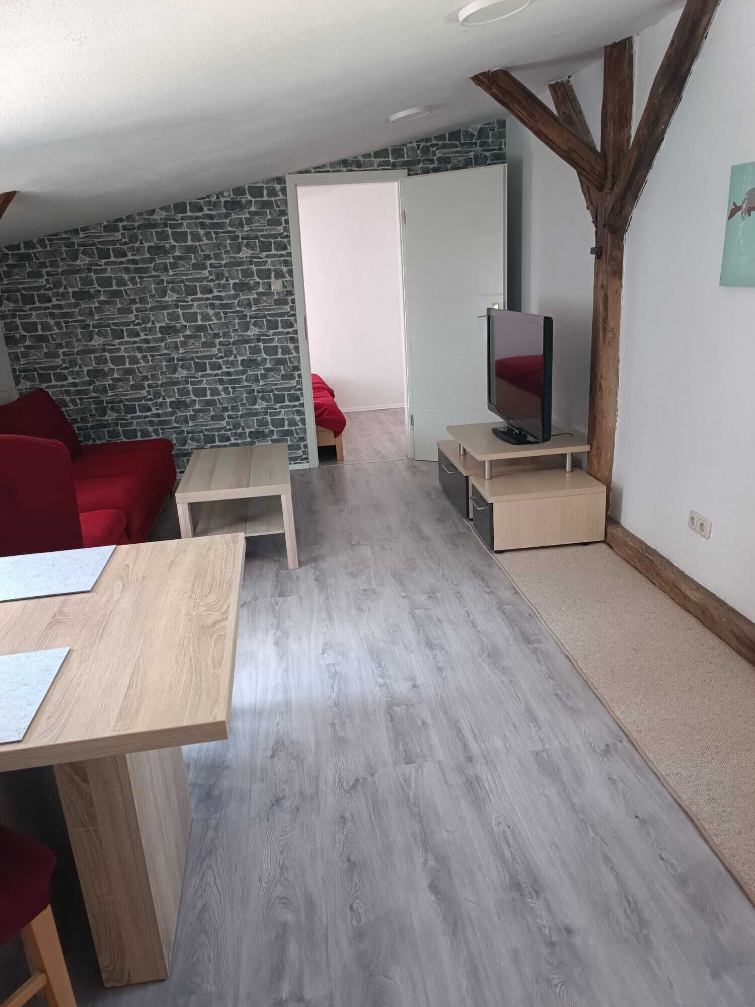 A modern living room with a stone wall, a red sofa, a wooden coffee table, a TV on a stand, and a door leading to another room.