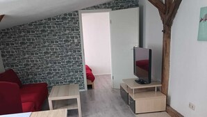 Een moderne woonkamer met een stenen muur, een rode bank, een houten salontafel, een tv op een meubelstuk, en een deur die naar een andere kamer leidt.