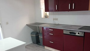 Een kleine keuken met een wit aanrecht, rode kastjes en een inbouwoven.