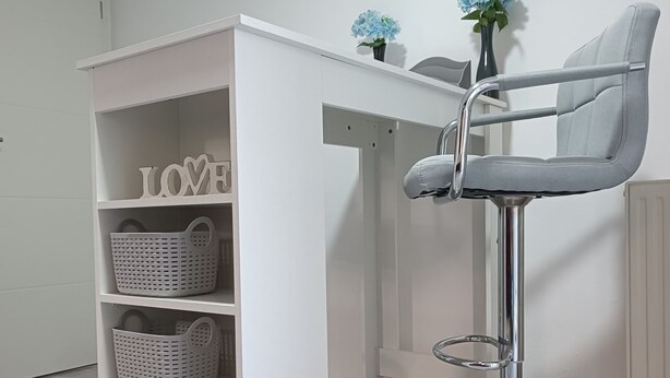 Een witte kamer met een wit bureau en een grijze stoel. Er staan manden op het bureau en een plank met de tekst 'LOVE'.