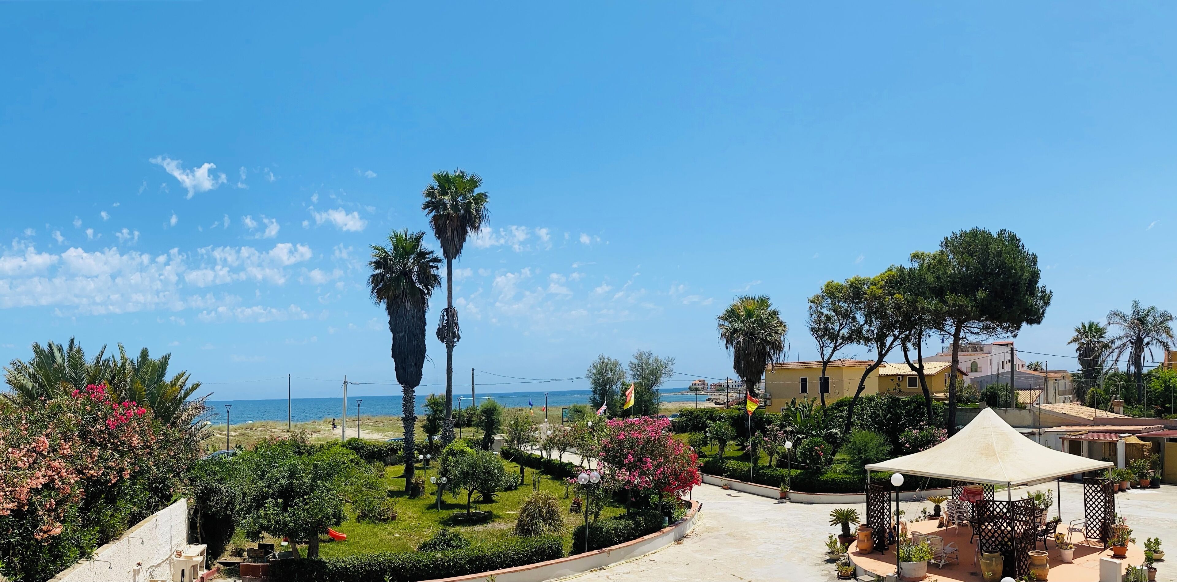 Ein sonniger Außenbereich mit einer Palme, einem Pavillon und Blick auf das Meer.