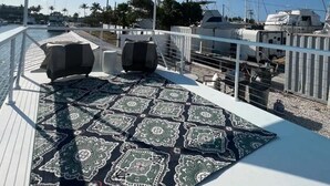 En takförsedd uteplats med ett mönstrat mattgolv, två bekväma fåtöljer och en utsikt över båtar och yachter i bakgrunden.