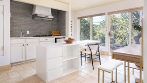Een moderne keuken met witte kastjes, een inbouwfornuis en een groot raam met uitzicht op bomen.