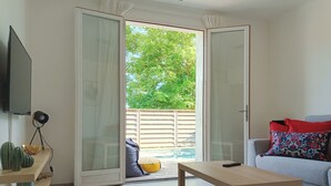 Ein Wohnzimmer mit Sofa, Couchtisch, Fernseher und einer Glastür, die zu einem Außenbereich mit Pool führt.