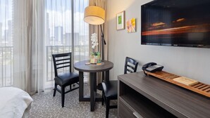 A hotel room with a bed, a desk with a telephone, a chair, a table with a lamp, and a TV on the wall. - Cozy Room in Heart of Waikiki (Honolulu)