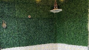 Une pièce avec un mur recouvert de feuilles vertes, une chaise à motifs floraux, une table en bois et un flacon contenant des tiges de roseau.