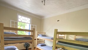 Une chambre de dortoir avec des lits superposés, une fenêtre et un ventilateur de plafond.