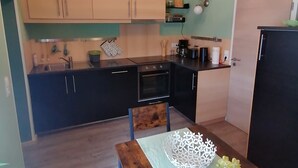 Une cuisine compacte avec des poutres en bois, une table à manger ornée d’un chemin de table en dentelle blanche et une petite plante en pot.