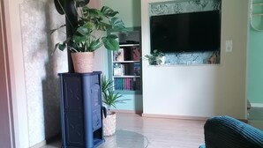 Un salon avec une table en bois, un canapé bleu, un téléviseur fixé au mur et une bibliothèque.