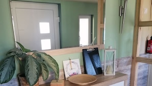 Une coiffeuse en bois avec un miroir, une plante en pot, un petit plateau en bois et un tableau encadré.