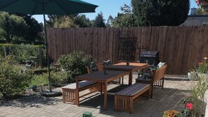 Une terrasse dotée de meubles en bois, d’un parasol vert et de plantes en pot.
