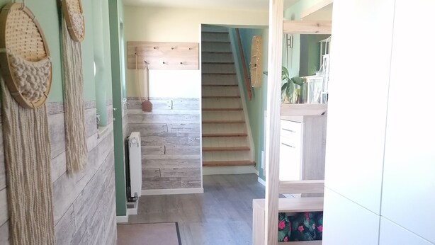 Un escalier menant à un deuxième étage, avec des finitions en bois, un meuble blanc sur la droite et un mur orné de paniers tressés.