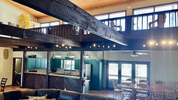 A spacious living area with a high ceiling, a wooden staircase, a kitchen with teal cabinets, and a dining area with wooden chairs. - Largest Cabin Available for Rent in Cucahra! 26+ (La Veta)