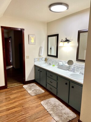 A bathroom with two sinks, a large mirror, and a ceiling light. There are wooden floors and two rugs. - Largest Cabin Available for Rent in Cucahra! 26+ (La Veta)
