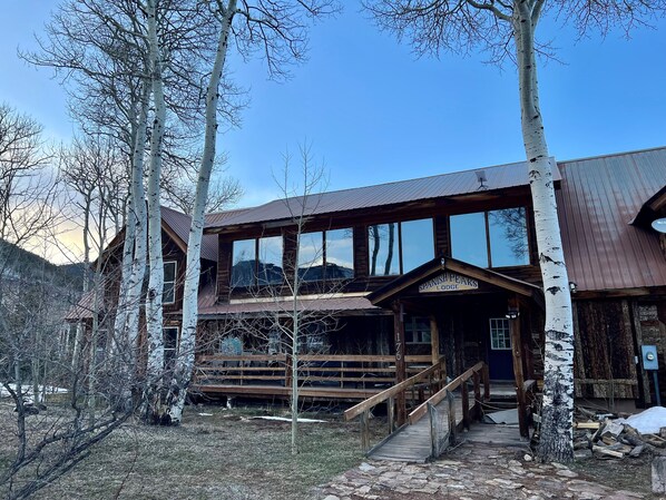A wooden lodge with a large windowed upper level and a wooden deck. - Largest Cabin Available for Rent in Cucahra! 26+ (La Veta)