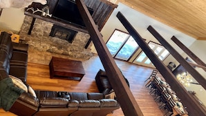 A spacious living area with a stone fireplace, leather sofa, and a dining area with wooden chairs and a chandelier. - Largest Cabin Available for Rent in Cucahra! 26+ (La Veta)