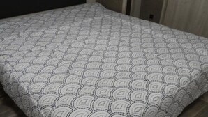 A neatly made bed with a patterned bedspread in a room with wooden walls and a dark headboard.