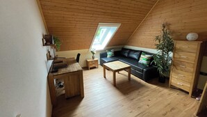 A cozy loft bedroom with a sloped ceiling, wooden walls, a black leather sofa, a wooden desk, and a large window. - Black Forest chic gallery apartment with high-quality furnishings - Mein SWH (Todtmoos)