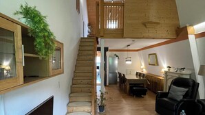 A spacious living area with a wooden staircase, a flat-screen TV, a dining table, and a leather sofa. - Black Forest chic gallery apartment with high-quality furnishings - Mein SWH (Todtmoos)