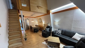 A modern living room with a wooden staircase, a black leather sofa, a dining area, and a kitchen. - Black Forest chic gallery apartment with high-quality furnishings - Mein SWH (Todtmoos)