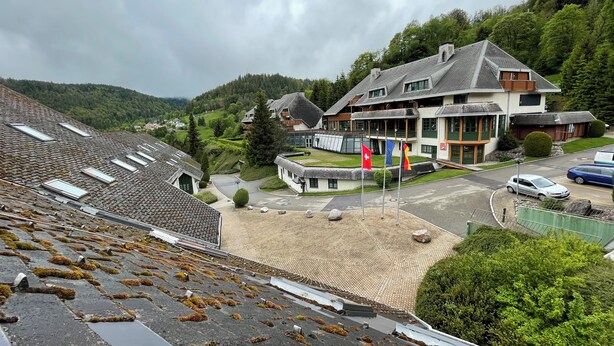 A building with a sloped roof, multiple windows, and flags. - Black Forest chic gallery apartment with high-quality furnishings - Mein SWH (Todtmoos)