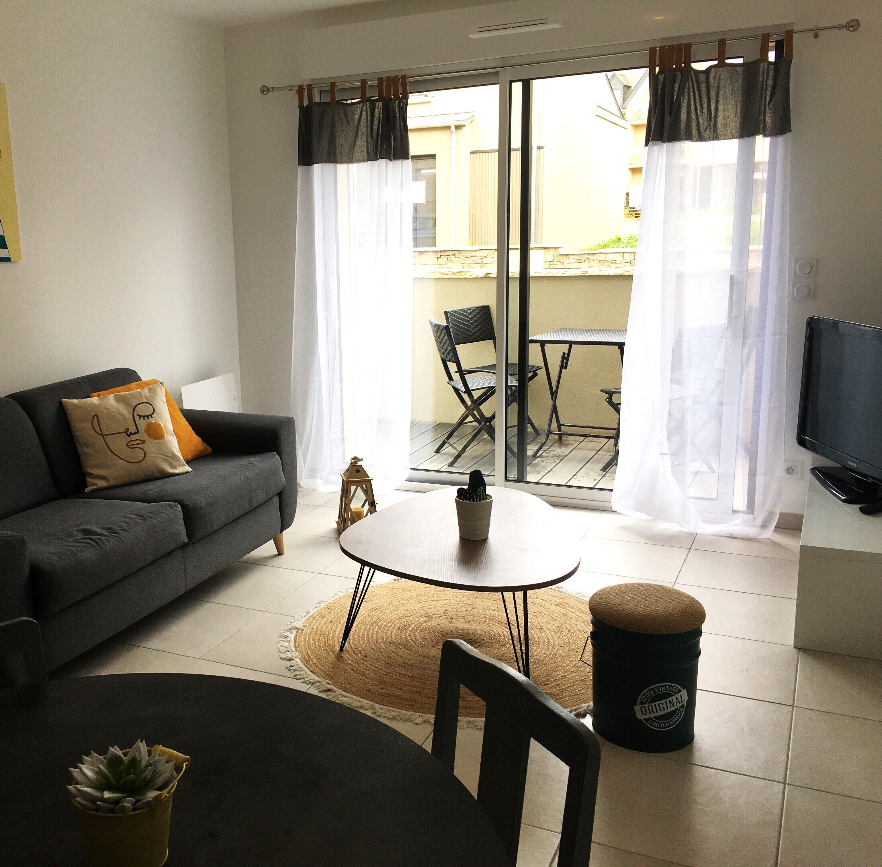 A living room with a sofa, a table, chairs, a TV, and a view through a glass door.