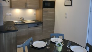 Eine moderne Küche mit Holzausstattung, einem Einbauofen und einem Geschirrspüler. Ein Esstisch mit Stühlen und Tellern steht dort, daneben ein kleiner Blumentopf.